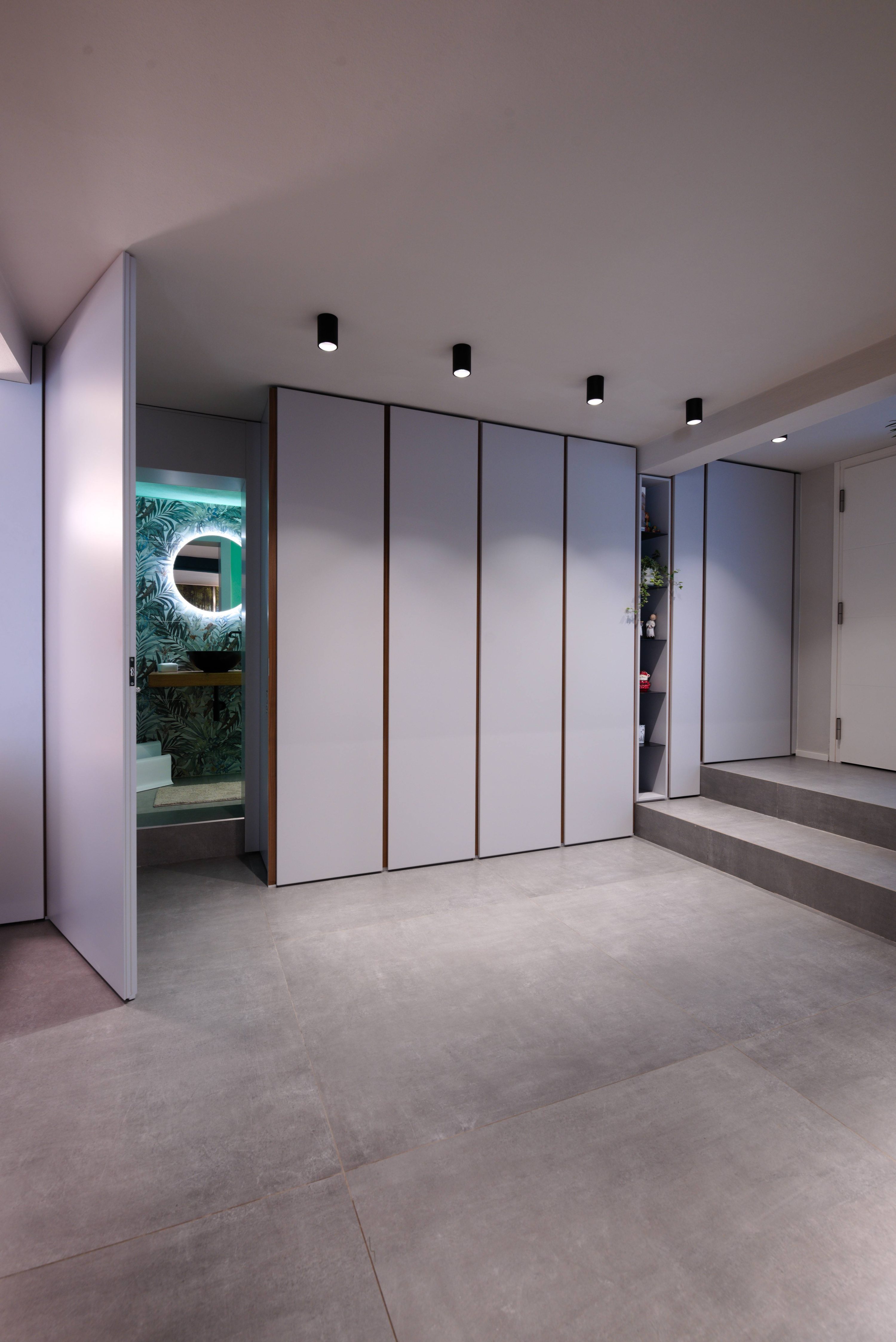 Armadio a muro aperto che rivela un passaggio segreto verso un bagno moderno con carta da parati tropicale e specchio retroilluminato. – MICHELE VOLPI STUDIO INTERIOR DESIGN Porta Integrata a Scomparsa e Bagno con gres effetto parati, stile Jungle